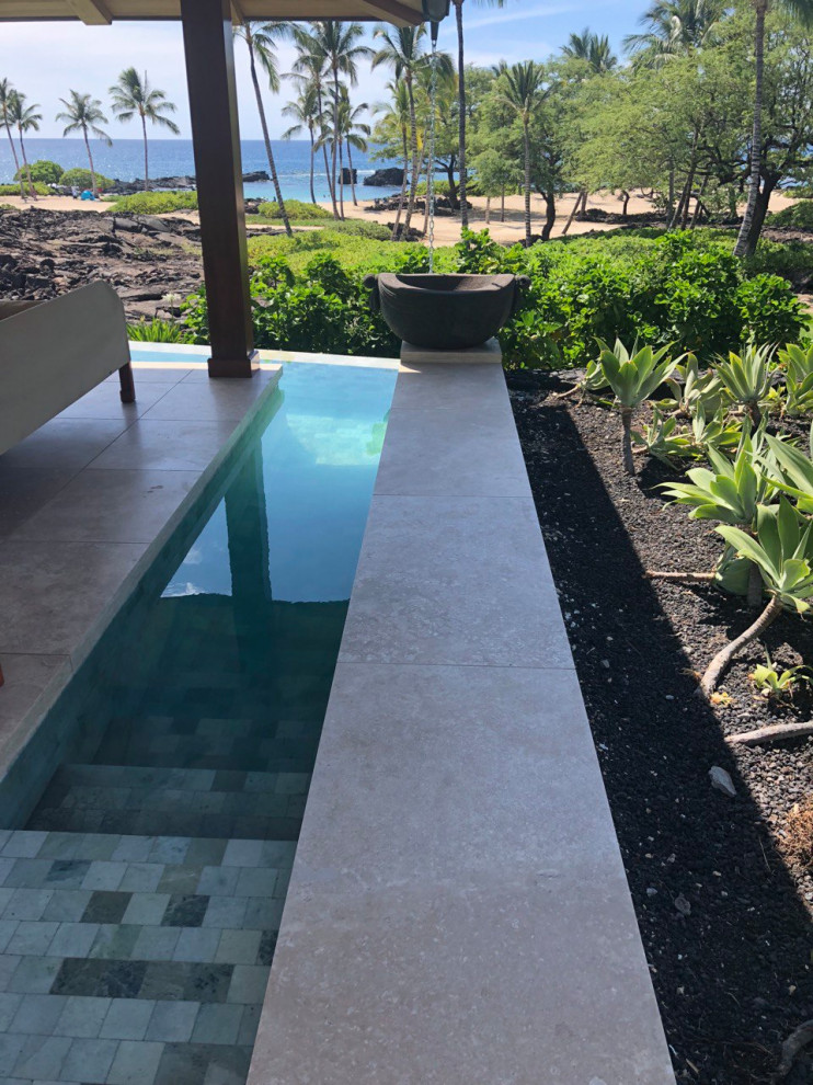 Immagine di una grande piscina tropicale a "L" davanti casa con paesaggistica bordo piscina e pavimentazioni in pietra naturale
