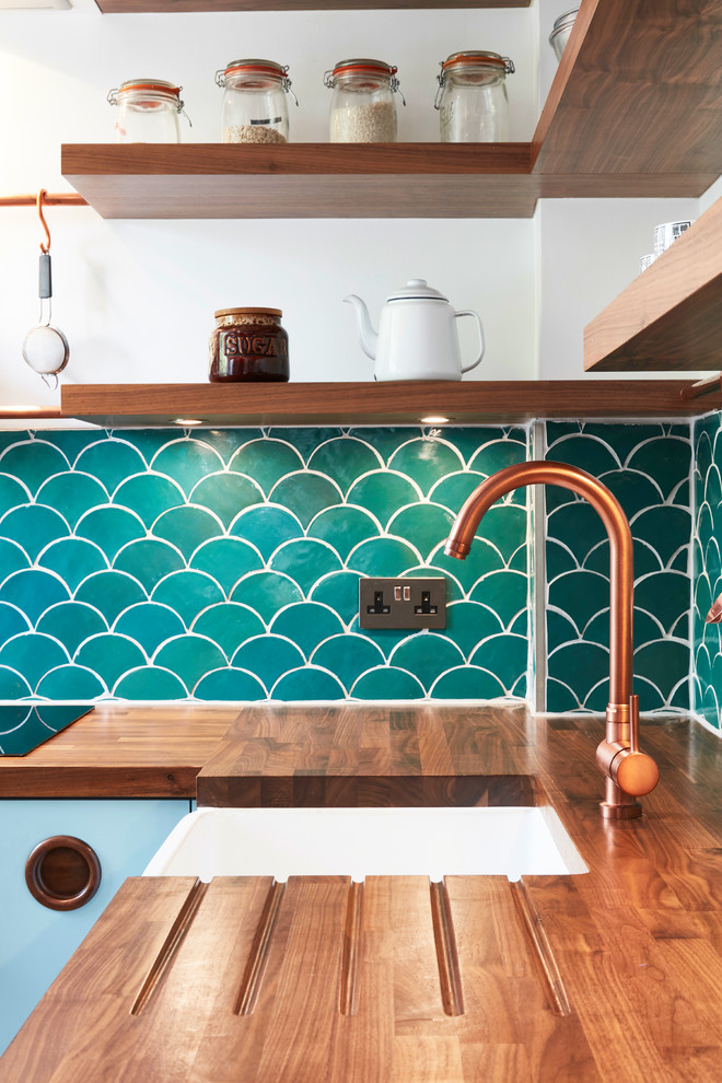 Photo of a small midcentury u-shaped separate kitchen in London with a farmhouse sink, flat-panel cabinets, blue cabinets, wood benchtops, blue splashback, cement tile splashback, stainless steel appliances, dark hardwood floors, no island and brown floor.