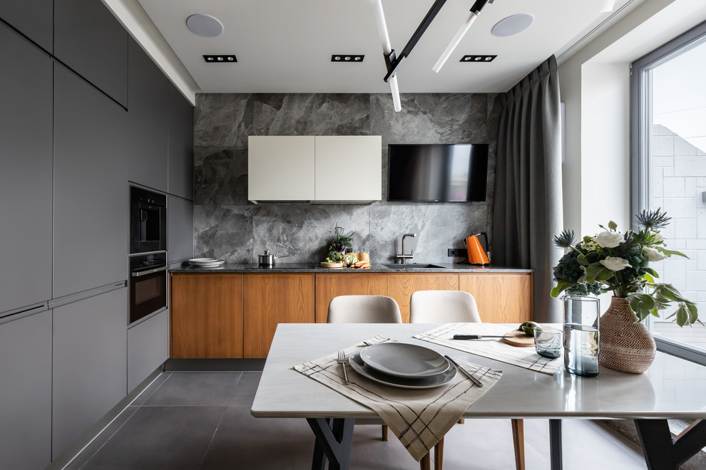 Design ideas for a contemporary l-shaped kitchen in Saint Petersburg with an undermount sink, flat-panel cabinets, white cabinets, solid surface benchtops, grey splashback, porcelain splashback, black appliances, porcelain floors, grey floor and grey benchtop.