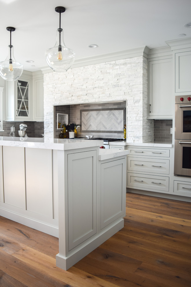 Inspiration for a mid-sized beach style u-shaped eat-in kitchen in New York with an undermount sink, shaker cabinets, grey cabinets, quartz benchtops, grey splashback, slate splashback, panelled appliances, medium hardwood floors and with island.