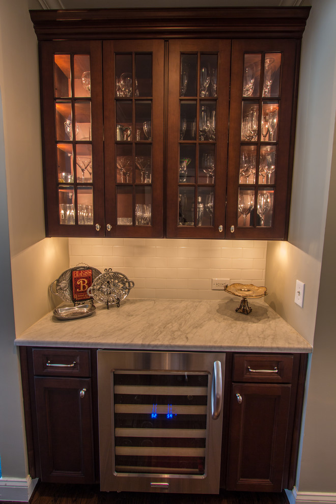 Design ideas for a small traditional single-wall wet bar in Atlanta with dark wood cabinets, marble benchtops, white splashback, ceramic splashback, no sink, glass-front cabinets and dark hardwood floors.