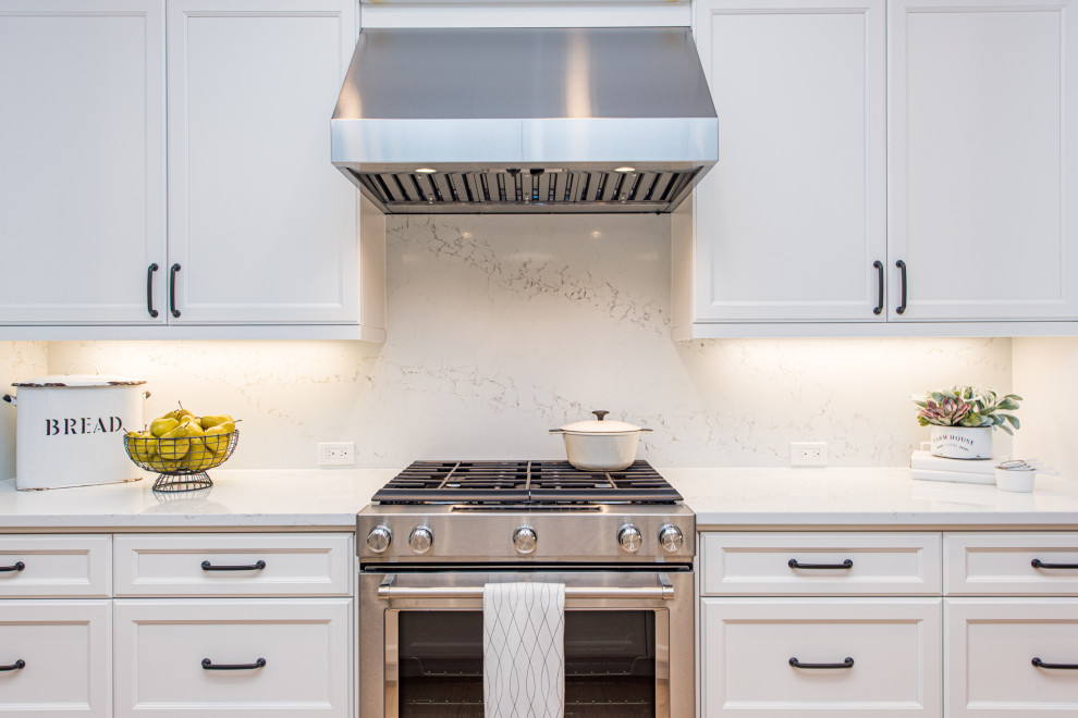 Example of a l-shaped light wood floor and brown floor open concept kitchen design in Seattle with a farmhouse sink, recessed-panel cabinets, white cabinets, quartz countertops, white backsplash, stainless steel appliances, an island and white countertops