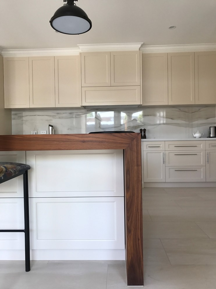 Design ideas for a large traditional galley open plan kitchen in Melbourne with a farmhouse sink, shaker cabinets, beige cabinets, wood benchtops, white splashback, porcelain splashback, black appliances and with island.
