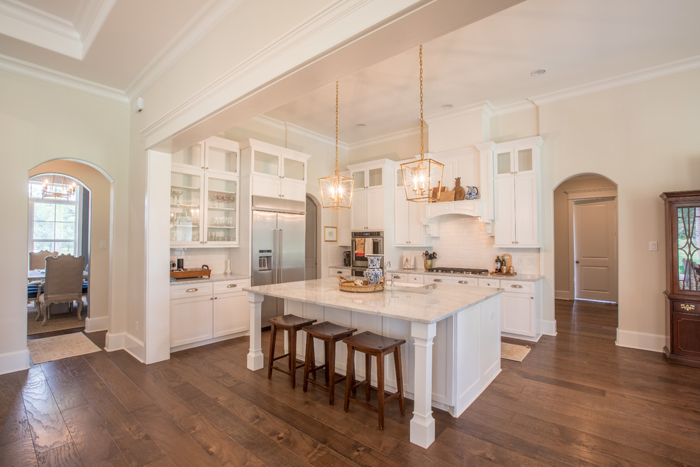 Inspiration for a large traditional l-shaped open plan kitchen in Houston with a farmhouse sink, dark hardwood floors, brown floor, shaker cabinets, white cabinets, quartzite benchtops, white splashback, subway tile splashback, stainless steel appliances, with island and white benchtop.