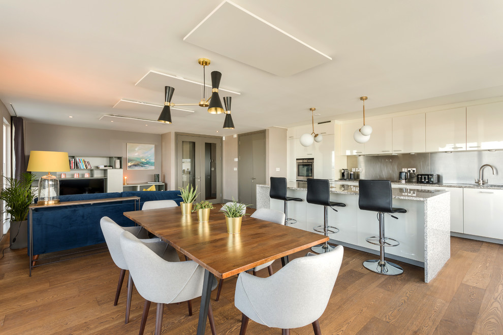 Design ideas for a mid-sized contemporary single-wall open plan kitchen in Dublin with an integrated sink, flat-panel cabinets, white cabinets, quartzite benchtops, metallic splashback, metal splashback, stainless steel appliances, medium hardwood floors, with island, brown floor and grey benchtop.