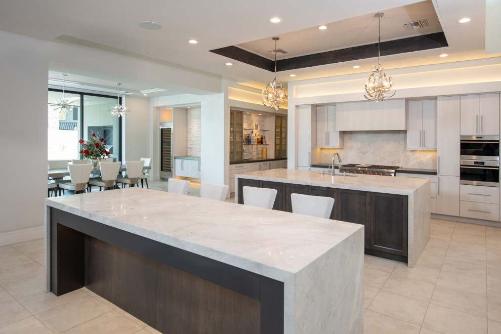 Inspiration for a large modern galley open plan kitchen in Phoenix with a drop-in sink, flat-panel cabinets, beige cabinets, marble benchtops, white splashback, marble splashback, stainless steel appliances, ceramic floors, multiple islands, beige floor, white benchtop and recessed.