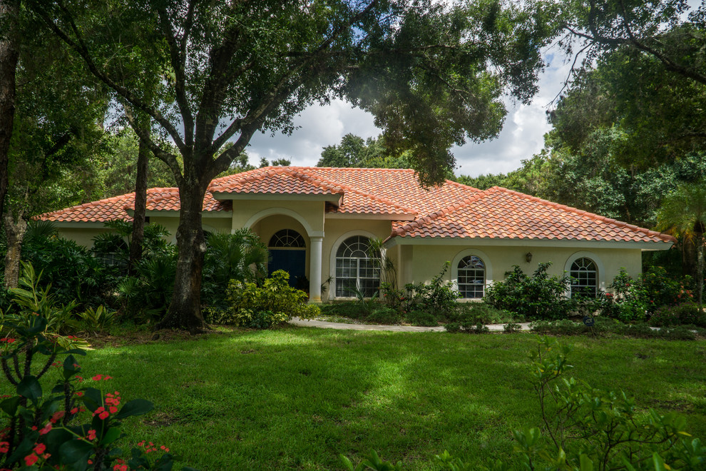 This is an example of a large transitional one-storey stucco beige house exterior in Tampa with a hip roof and a tile roof.