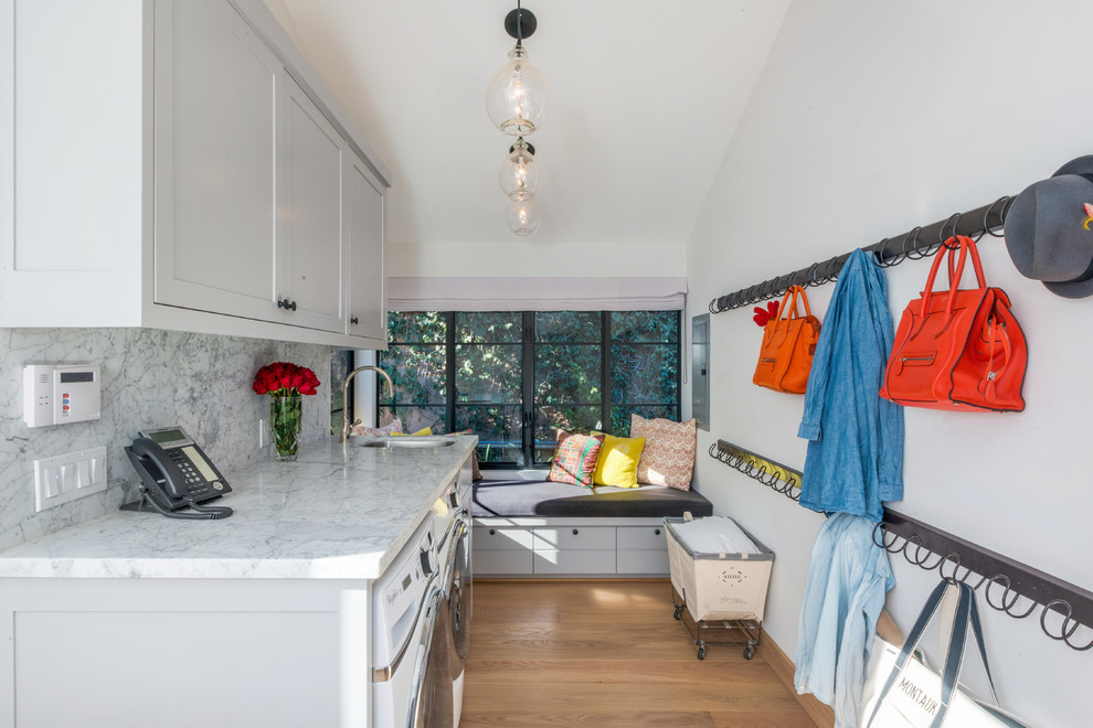 Photo of a large contemporary galley dedicated laundry room in Los Angeles with recessed-panel cabinets, white cabinets, marble benchtops, white walls, light hardwood floors, a side-by-side washer and dryer, brown floor, white benchtop and an undermount sink.