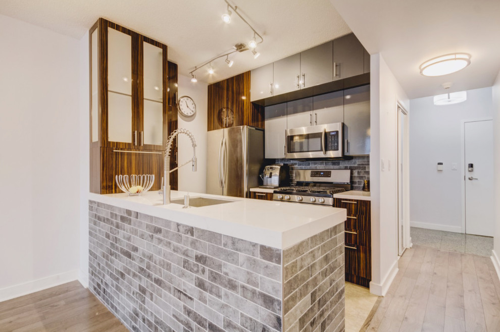 Inspiration for a mid-sized modern galley open plan kitchen in Toronto with an undermount sink, flat-panel cabinets, brown cabinets, quartz benchtops, grey splashback, cement tile splashback, stainless steel appliances, plywood floors, a peninsula, grey floor and white benchtop.