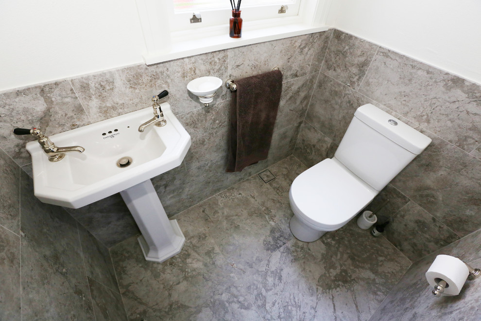 This is an example of a small contemporary bathroom in Sydney with a two-piece toilet, gray tile, stone tile, white walls, limestone floors and a console sink.