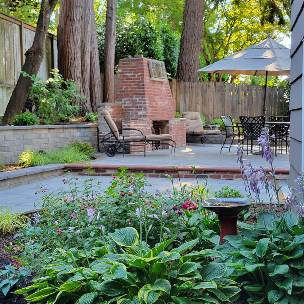 На фото: большой летний регулярный сад на заднем дворе в классическом стиле с уличным камином, полуденной тенью и мощением тротуарной плиткой