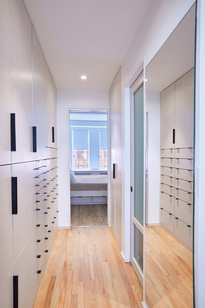 This is an example of a small contemporary gender neutral dressing room in New York with flat-panel cabinets, grey cabinets, light hardwood flooring and beige floors.