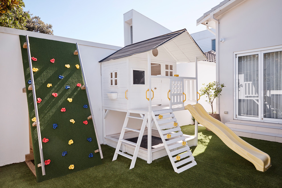 This is an example of a large beach style backyard garden for summer in Sydney with with outdoor playset.