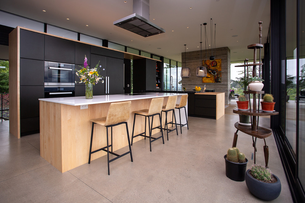 Modern l-shaped eat-in kitchen in Portland with flat-panel cabinets, black cabinets, wood benchtops, with island, a drop-in sink, panelled appliances, concrete floors, grey floor and white benchtop.