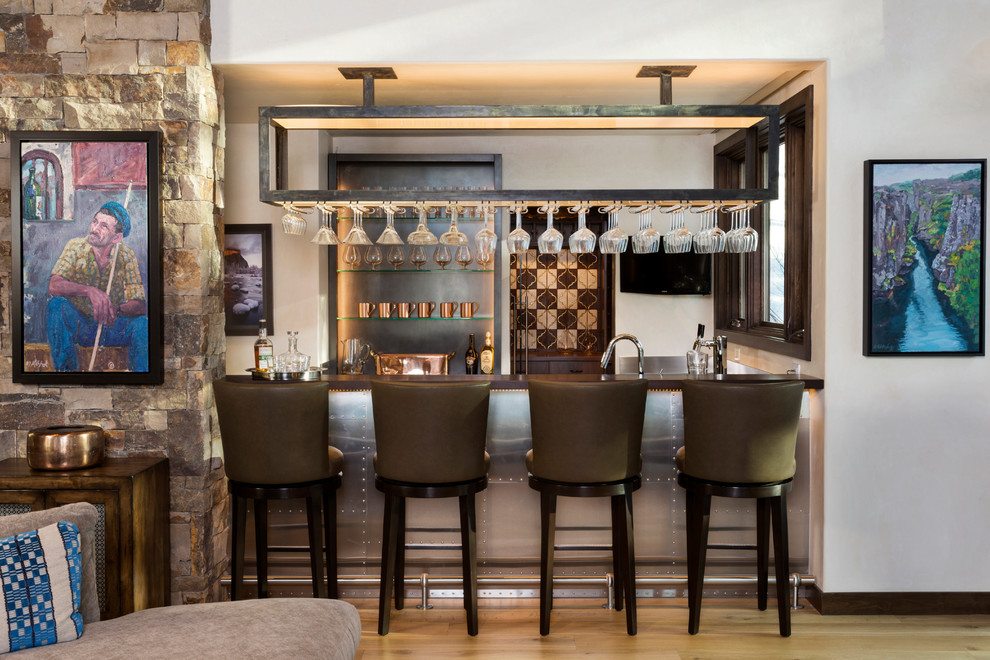 This is an example of a small country u-shaped seated home bar in Denver with an undermount sink, stainless steel benchtops and medium hardwood floors.