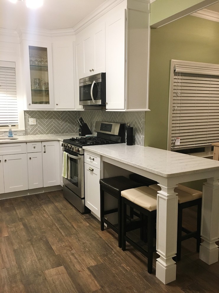 Photo of a mid-sized country u-shaped eat-in kitchen in New York with an undermount sink, shaker cabinets, white cabinets, quartz benchtops, grey splashback, glass tile splashback, porcelain floors, a peninsula and brown floor.