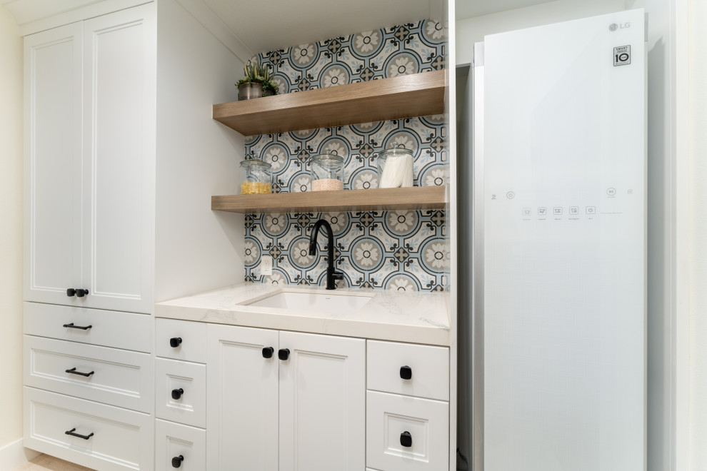 Mid-sized country galley dedicated laundry room in Orange County with an undermount sink, recessed-panel cabinets, white cabinets, quartz benchtops, multi-coloured splashback, cement tile splashback, white walls, limestone floors, a side-by-side washer and dryer, beige floor and white benchtop.