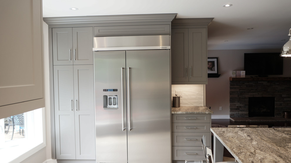 Example of a large transitional u-shaped kitchen design in Toronto with a single-bowl sink, shaker cabinets, white cabinets, granite countertops, white backsplash, porcelain backsplash, stainless steel appliances and an island