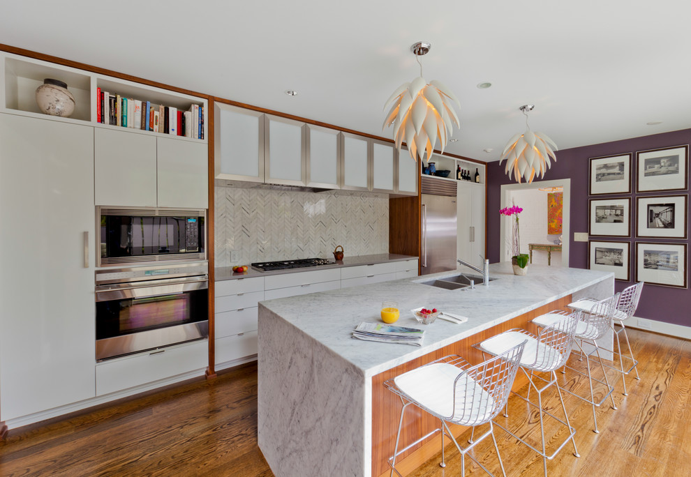 This is an example of a modern galley separate kitchen in Charlotte with a double-bowl sink, flat-panel cabinets, white cabinets, white splashback, stone tile splashback and stainless steel appliances.