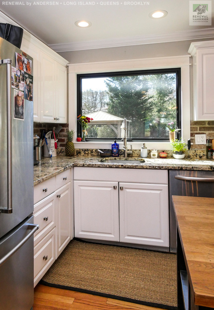 This is an example of a mid-sized l-shaped eat-in kitchen in New York with an undermount sink, white cabinets, granite benchtops, beige splashback, brick splashback, stainless steel appliances, medium hardwood floors, with island and multi-coloured benchtop.