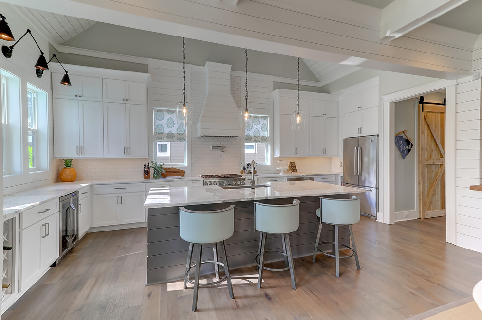 This is an example of a large contemporary u-shaped open plan kitchen in Charleston with white cabinets, marble benchtops, white splashback, glass tile splashback, stainless steel appliances, light hardwood floors, with island and brown floor.
