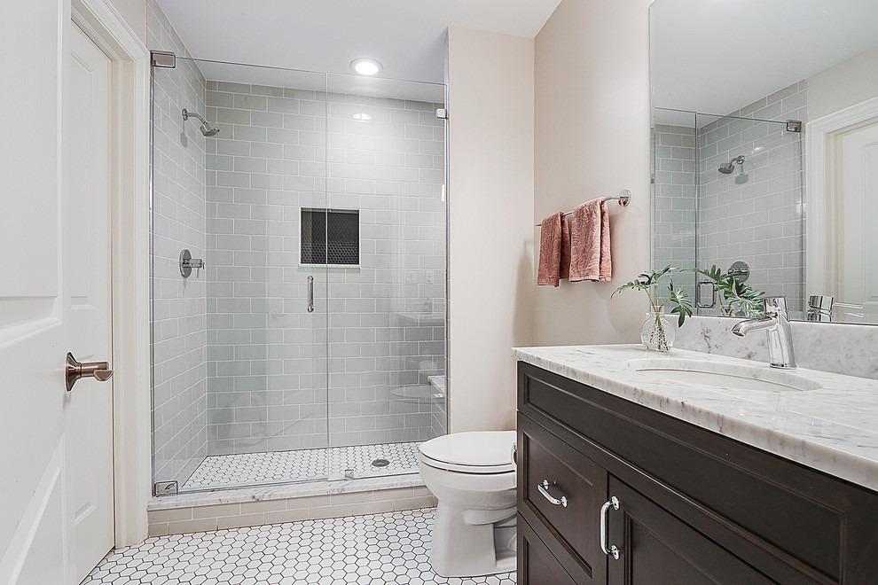 Design ideas for a mid-sized transitional bathroom in Chicago with raised-panel cabinets, dark wood cabinets, a freestanding tub, an alcove shower, a one-piece toilet, beige tile, mirror tile, white walls, ceramic floors, an undermount sink, engineered quartz benchtops, grey floor, a hinged shower door and grey benchtops.