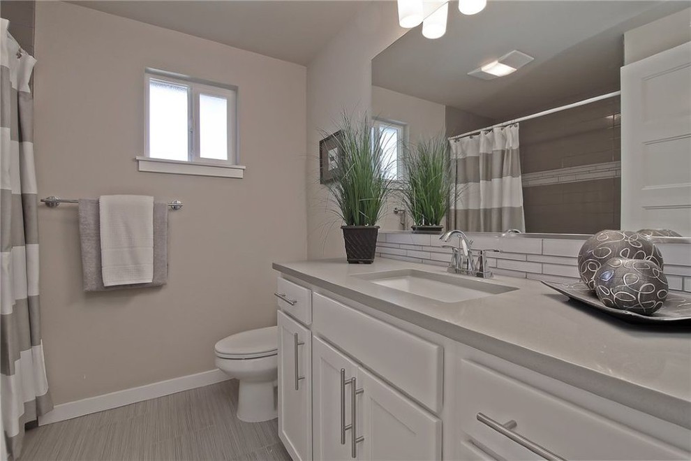 Mid-sized midcentury 3/4 bathroom in Seattle with shaker cabinets, white cabinets, a drop-in tub, a two-piece toilet, gray tile, glass tile, beige walls, ceramic floors, an undermount sink, quartzite benchtops, grey floor, a hinged shower door and grey benchtops.