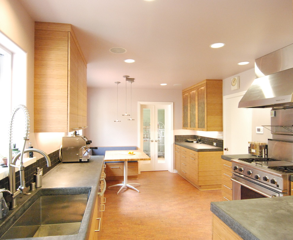 Photo of a mid-sized contemporary galley eat-in kitchen in San Francisco with a single-bowl sink, flat-panel cabinets, medium wood cabinets, solid surface benchtops, grey splashback, stainless steel appliances, cork floors and stone slab splashback.