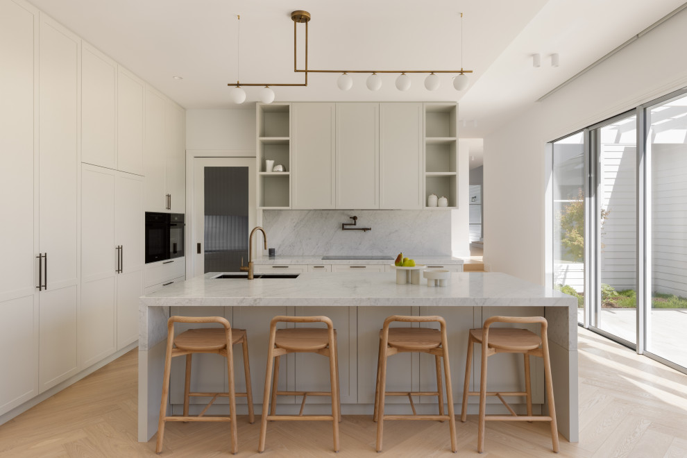 Inspiration for a contemporary l-shaped kitchen in Melbourne with an undermount sink, shaker cabinets, white cabinets, white splashback, stone slab splashback, black appliances, light hardwood floors, with island, beige floor and white benchtop.