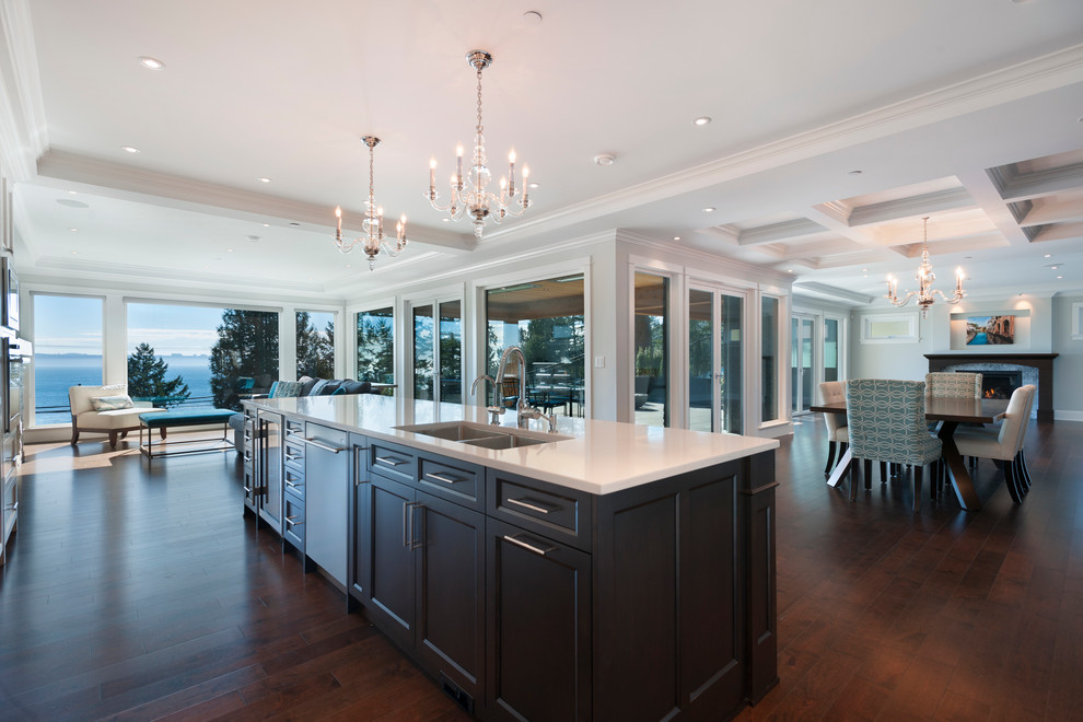 Photo of an expansive transitional l-shaped open plan kitchen in Vancouver with an undermount sink, shaker cabinets, white cabinets, marble benchtops, white splashback, stone tile splashback, white appliances, medium hardwood floors and with island.