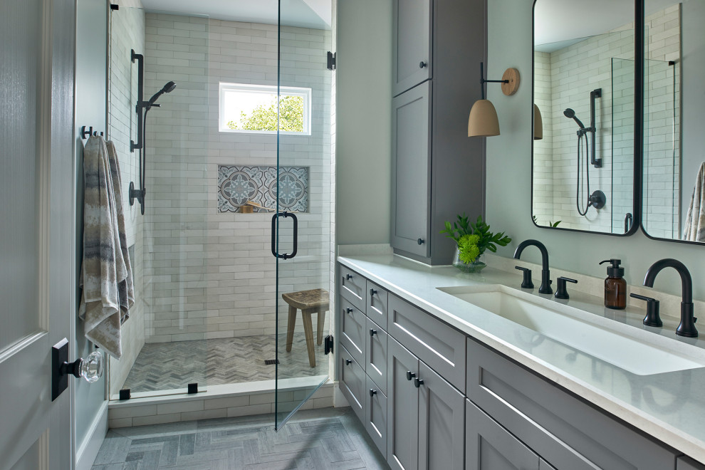 Inredning av ett klassiskt vit vitt badrum, med grå skåp, våtrum, beige kakel, ett avlångt handfat, grått golv och med dusch som är öppen