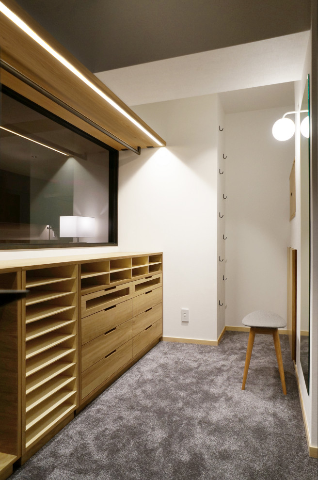 Inredning av ett minimalistiskt walk-in-closet för könsneutrala, med öppna hyllor, skåp i ljust trä, heltäckningsmatta och grått golv