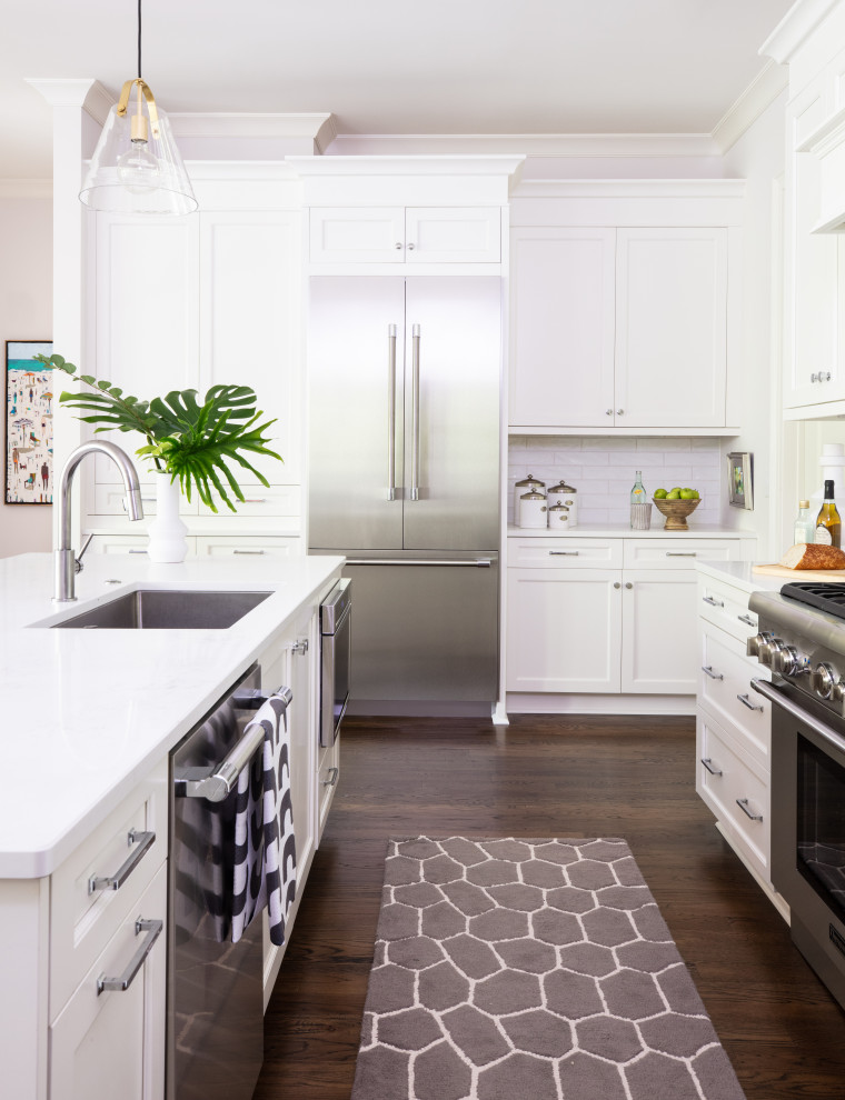 Inspiration for a classic u-shaped kitchen pantry in Raleigh with a single-bowl sink, shaker cabinets, white cabinets, engineered stone countertops, white splashback, ceramic splashback, stainless steel appliances, dark hardwood flooring, an island and white worktops.