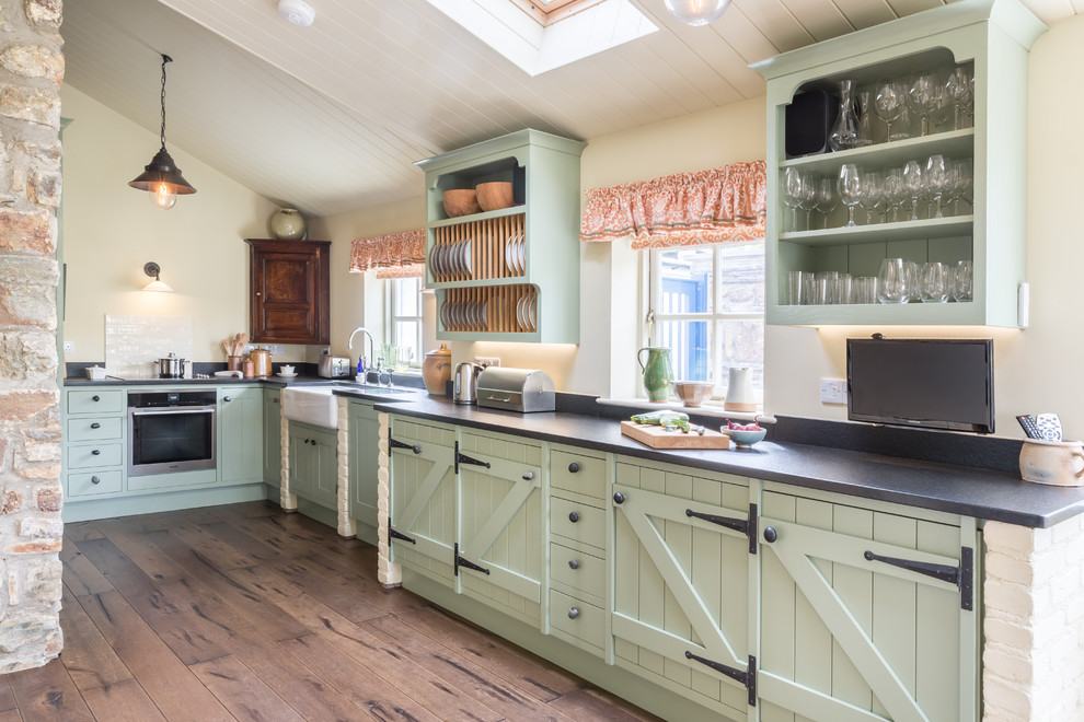 Inspiration for a country kitchen in Other with a farmhouse sink, green cabinets, black appliances, medium hardwood floors, no island and brown floor.