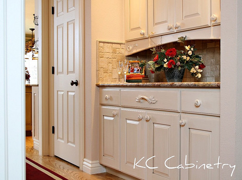 Photo of a mid-sized traditional l-shaped eat-in kitchen in Denver with a double-bowl sink, raised-panel cabinets, white cabinets, beige splashback, panelled appliances, light hardwood floors and with island.