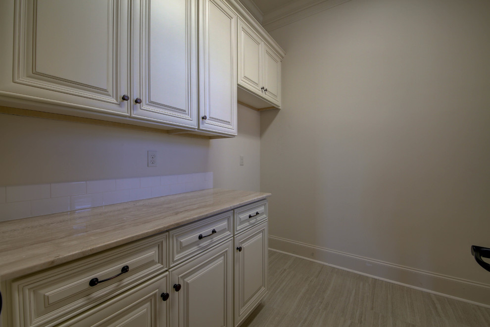 Photo of a mid-sized traditional laundry room in New Orleans with raised-panel cabinets, white cabinets, granite benchtops, white walls and porcelain floors.