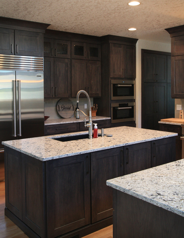Example of a large transitional u-shaped light wood floor eat-in kitchen design in Cedar Rapids with an undermount sink, shaker cabinets, dark wood cabinets, granite countertops, gray backsplash, glass tile backsplash, stainless steel appliances and an island