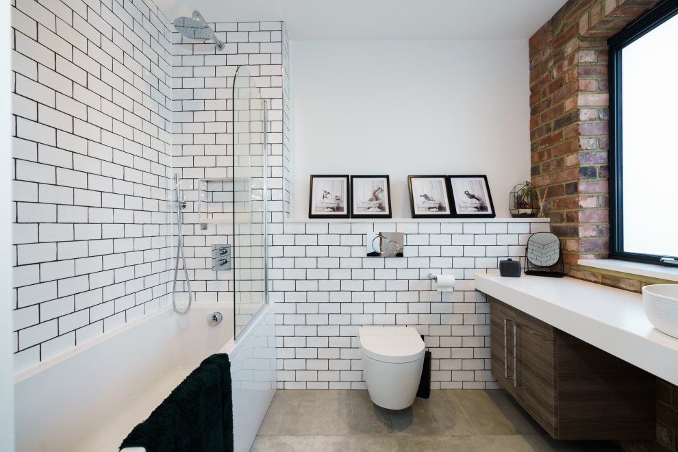 Contemporary bathroom in Buckinghamshire with flat-panel cabinets, dark wood cabinets, a shower/bath combination, white tiles, metro tiles, white walls, concrete flooring, a vessel sink, grey floors, an open shower, white worktops, a single sink and a floating vanity unit.