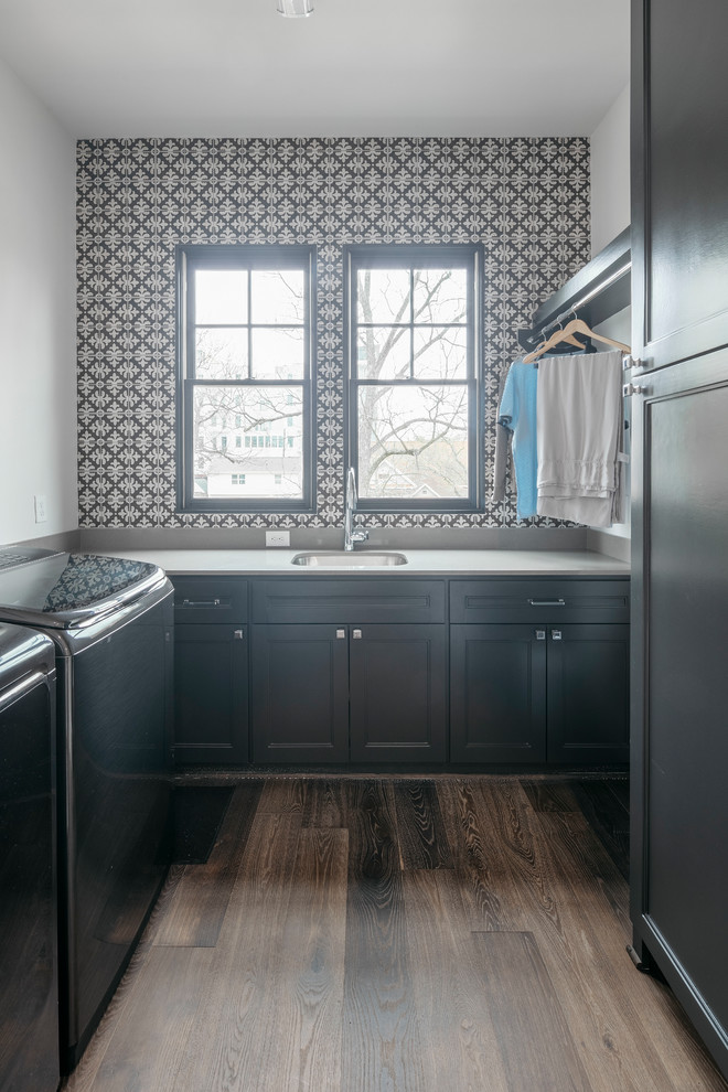 Mid-sized transitional galley dedicated laundry room in Houston with an undermount sink, recessed-panel cabinets, black cabinets, black walls, dark hardwood floors, a side-by-side washer and dryer, brown floor and white benchtop.