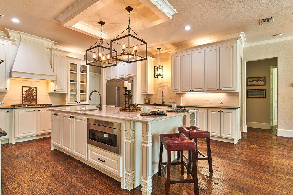 This is an example of a large traditional u-shaped open plan kitchen in Dallas with an undermount sink, raised-panel cabinets, white cabinets, granite benchtops, grey splashback, porcelain splashback, stainless steel appliances, medium hardwood floors, with island, brown floor and grey benchtop.