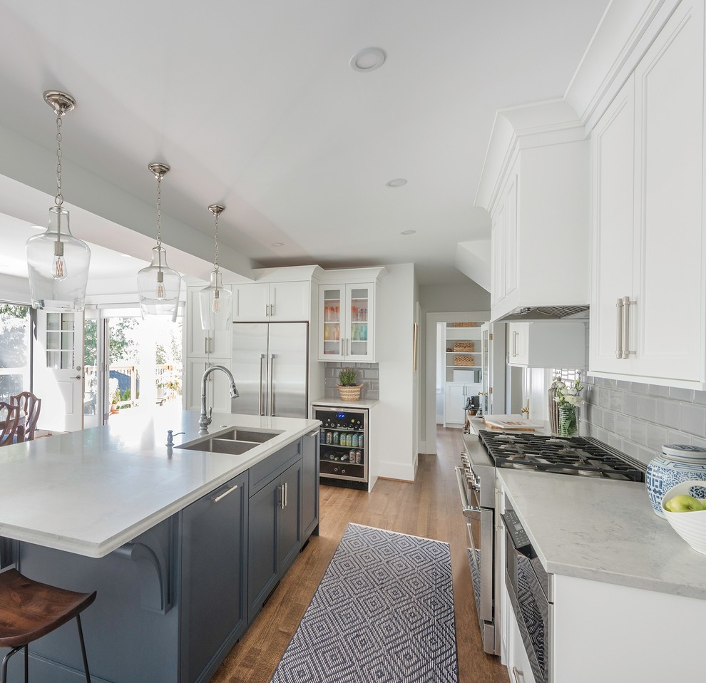 Photo of a large traditional u-shaped open plan kitchen in Vancouver with an undermount sink, recessed-panel cabinets, white cabinets, quartz benchtops, grey splashback, porcelain splashback, stainless steel appliances, medium hardwood floors, with island, brown floor and grey benchtop.