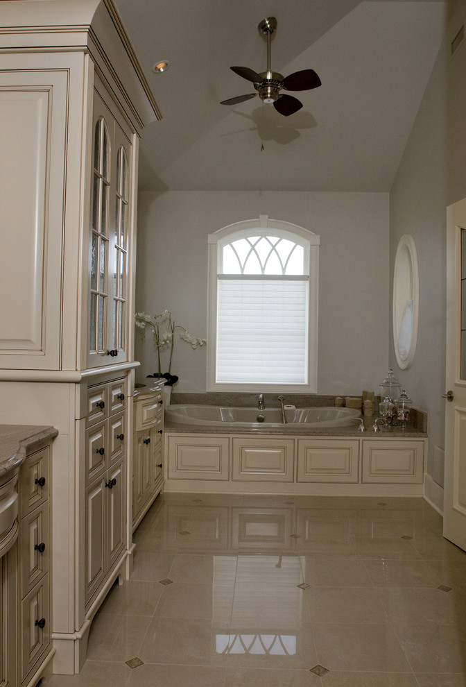 This is an example of a mid-sized traditional master bathroom in Wilmington with raised-panel cabinets, beige cabinets, a drop-in tub, an open shower, a one-piece toilet, beige tile, porcelain tile, beige walls, porcelain floors, a drop-in sink, granite benchtops, beige floor, a hinged shower door, beige benchtops, a shower seat, a double vanity, a built-in vanity and vaulted.