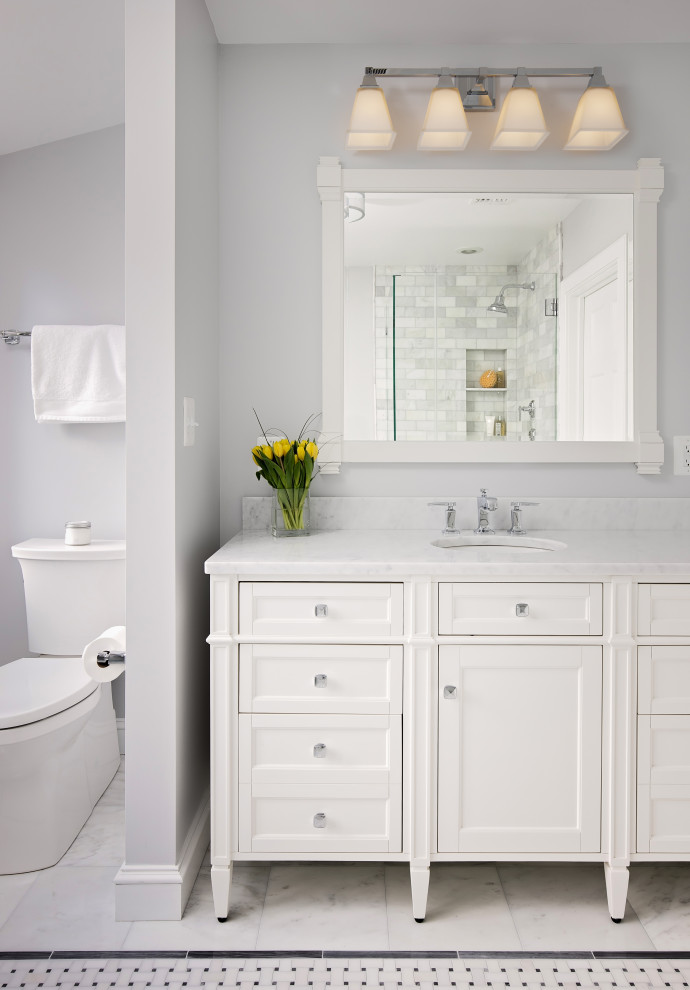 Photo of a large traditional master bathroom in DC Metro with a single vanity, recessed-panel cabinets, white cabinets, a drop-in tub, a corner shower, a two-piece toilet, gray tile, marble, grey walls, marble floors, an undermount sink, marble benchtops, grey floor, a hinged shower door, white benchtops, a niche and a freestanding vanity.