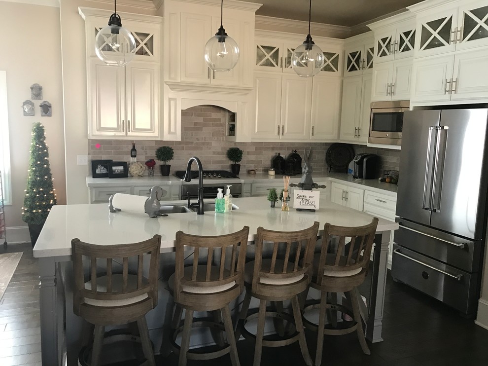 This is an example of a mid-sized country l-shaped open plan kitchen in Austin with a double-bowl sink, raised-panel cabinets, white cabinets, terrazzo benchtops, grey splashback, stone tile splashback, stainless steel appliances, dark hardwood floors and with island.