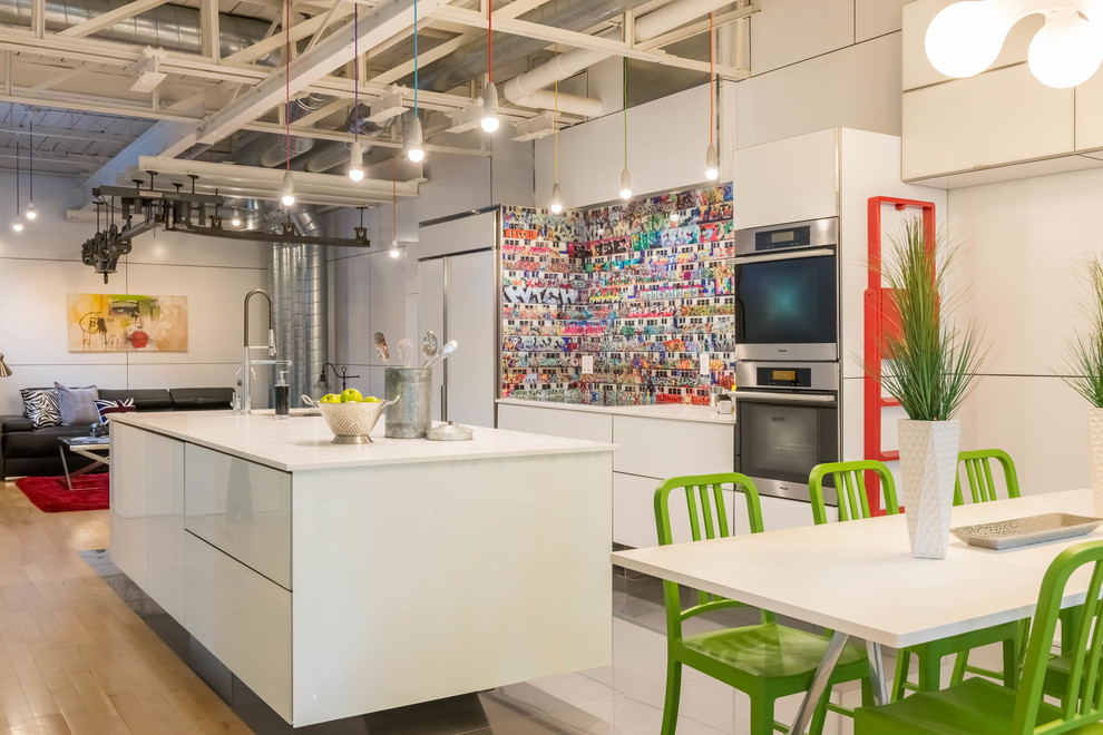 This is an example of an industrial kitchen in Toronto with an undermount sink, flat-panel cabinets, white cabinets, multi-coloured splashback, stainless steel appliances, light hardwood floors and with island.
