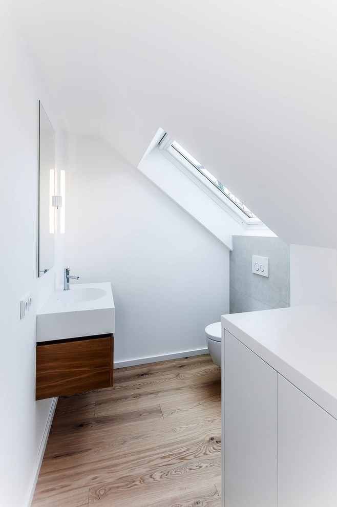 Photo of a small contemporary powder room in Munich with dark wood cabinets, a wall-mount toilet, gray tile, white walls, an integrated sink, wood benchtops, stone tile and medium hardwood floors.