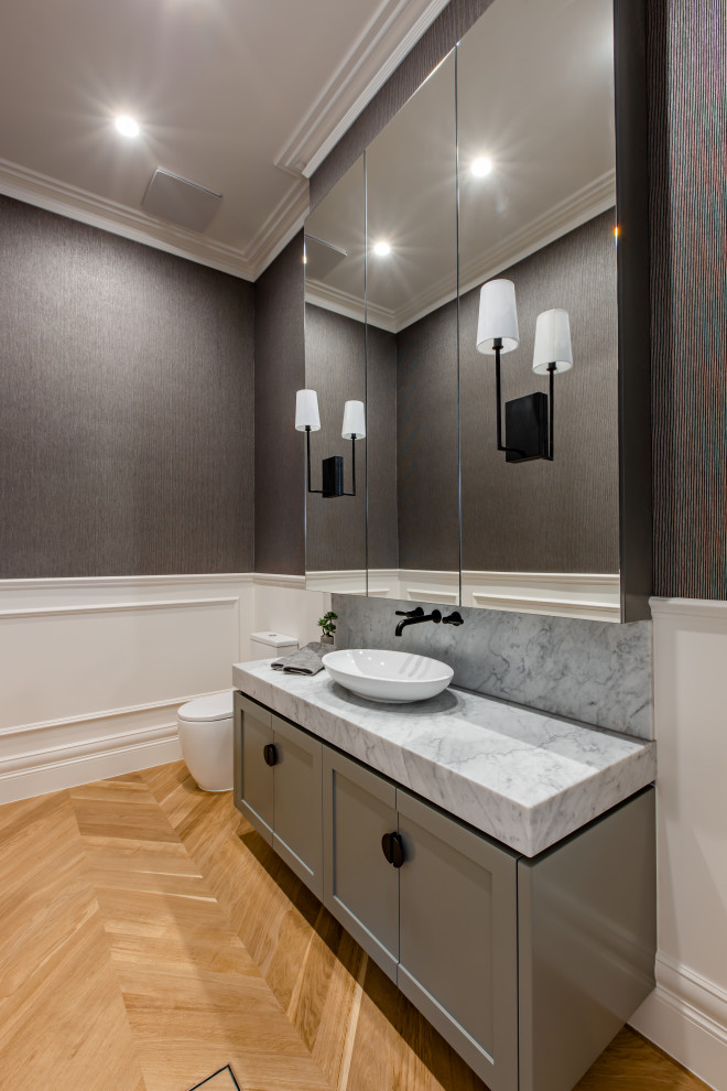 Inspiration for a traditional powder room in Adelaide with shaker cabinets, grey cabinets, a one-piece toilet, white walls, light hardwood floors, a vessel sink, engineered quartz benchtops and white benchtops.