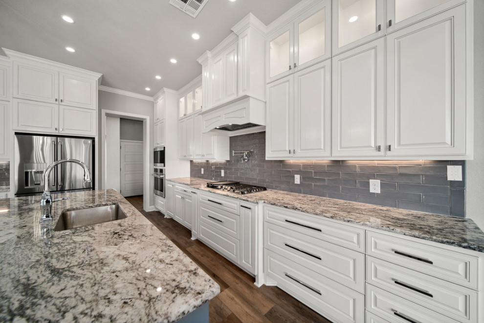Inspiration for a large traditional l-shaped open plan kitchen in Austin with a single-bowl sink, shaker cabinets, white cabinets, granite benchtops, grey splashback, porcelain splashback, stainless steel appliances, vinyl floors, with island, brown floor and brown benchtop.