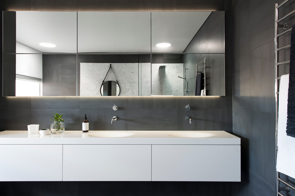 Photo of a large contemporary master bathroom in Sydney with an integrated sink, furniture-like cabinets, white cabinets, solid surface benchtops, a freestanding tub, an open shower, a one-piece toilet, gray tile, ceramic tile, grey walls and ceramic floors.