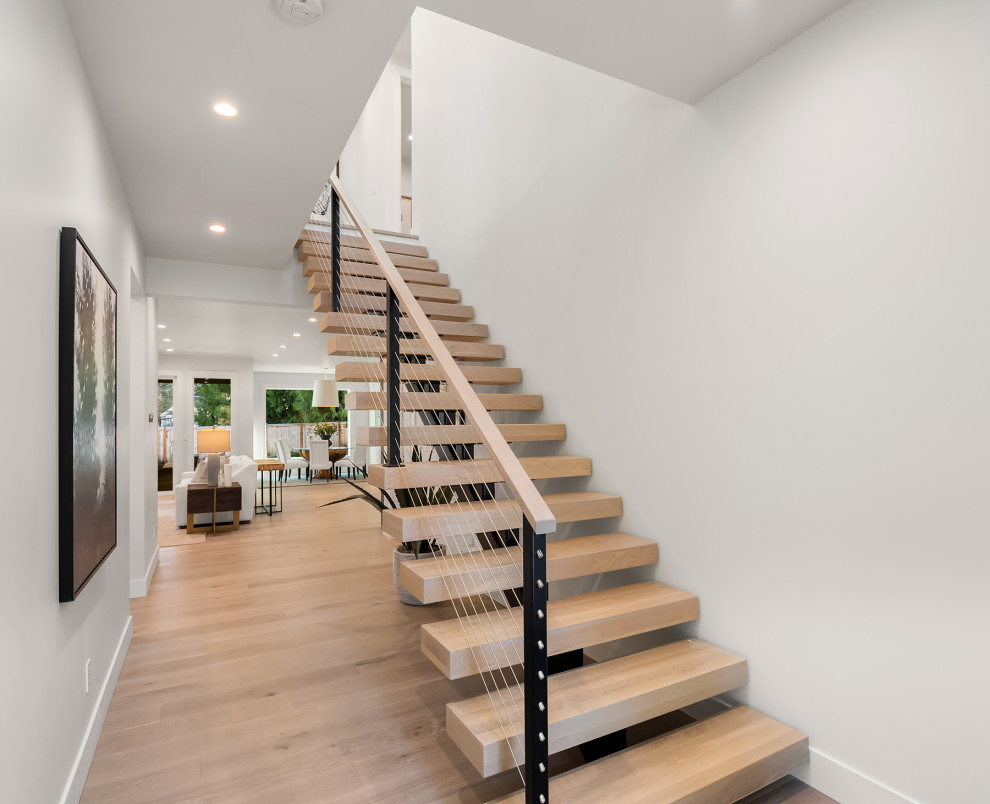 Ejemplo de escalera suspendida minimalista sin contrahuella con escalones de madera y barandilla de cable